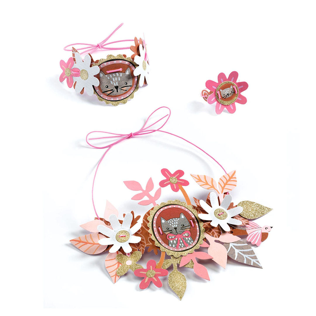 Een set van roze en witte bloemen sieraden met een kattenmotief, bestaande uit een ketting, armband en ring.