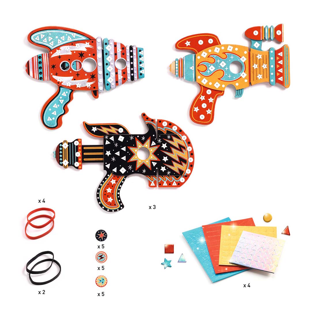Drie versierde mozaïek raketten/blasters met de bijbehorende knutselmaterialen zoals elastiekjes en stickers.