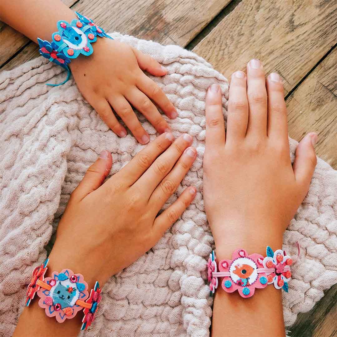 Twee kinderhanden dragen zelfgemaakte vilten armbandjes met bloemen en dieren.