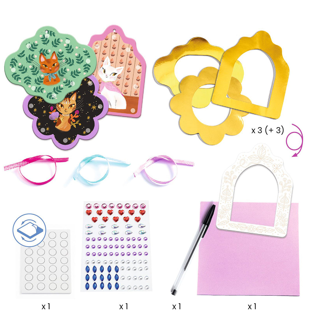Overzicht van de onderdelen van de Djeco knutselset met kattenportretten, metalen frames, lintjes en edelsteenstickers.