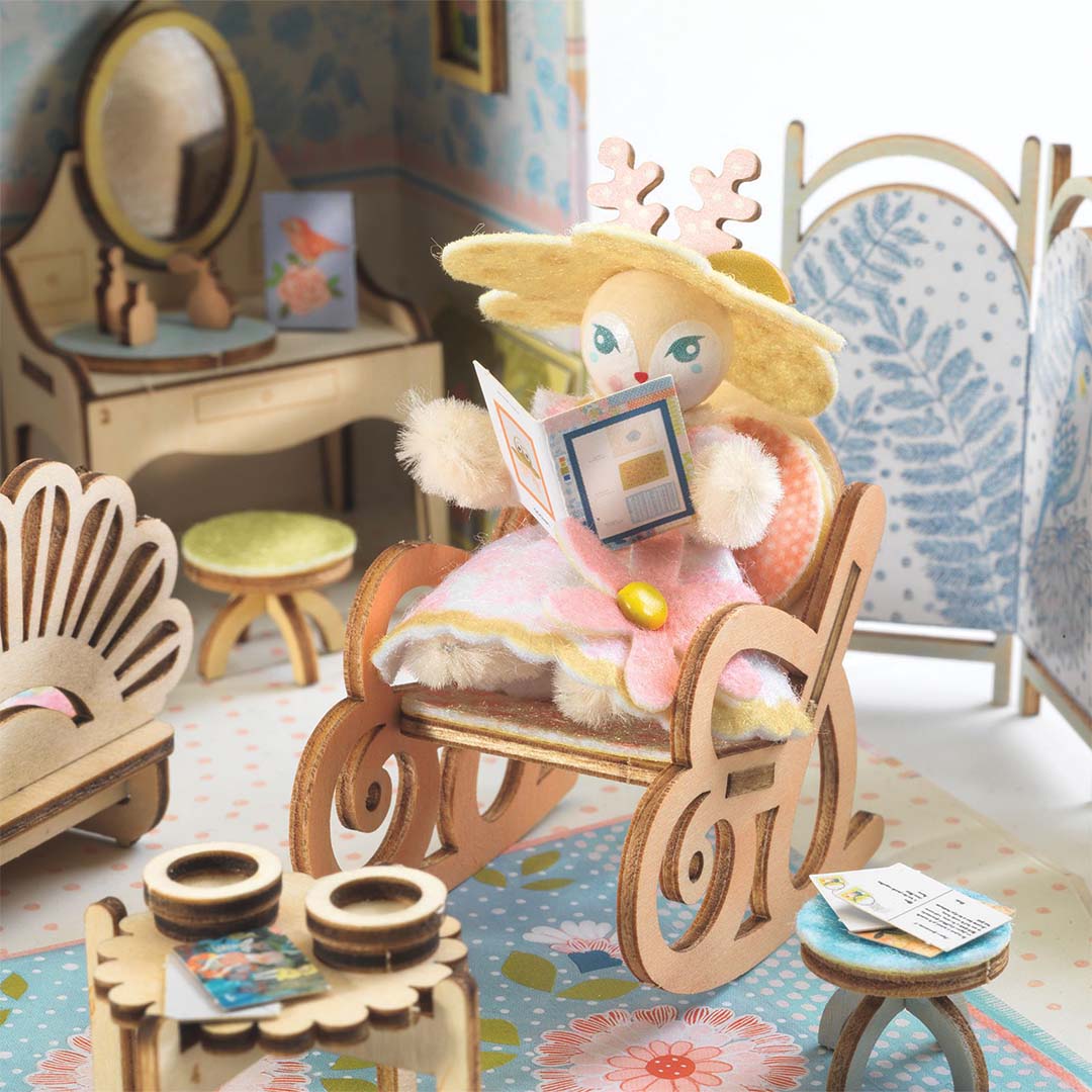Detail van het Alba poppenhuisje met een konijnfiguur dat in een houten schommelstoel een boekje leest.
