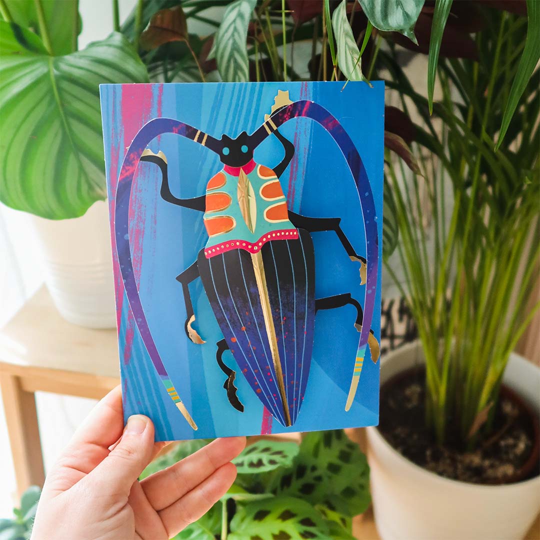 Een hand houdt een afgewerkt Djeco 3D-insectenkunstwerk vast met een blauwe achtergrond.