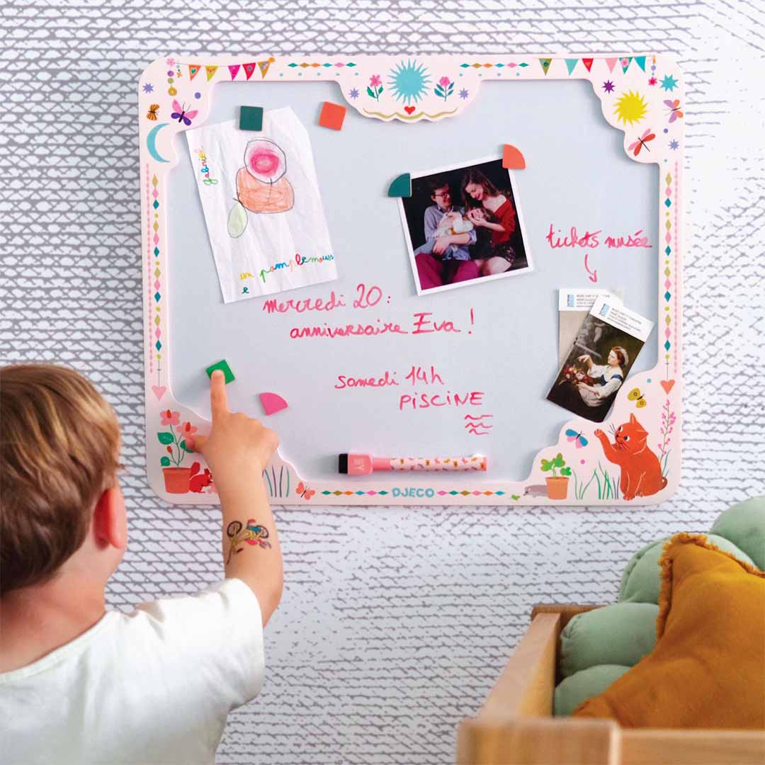 Een kind plaatst een magneet op het Djeco magnetisch tekenbord dat aan een muur hangt.