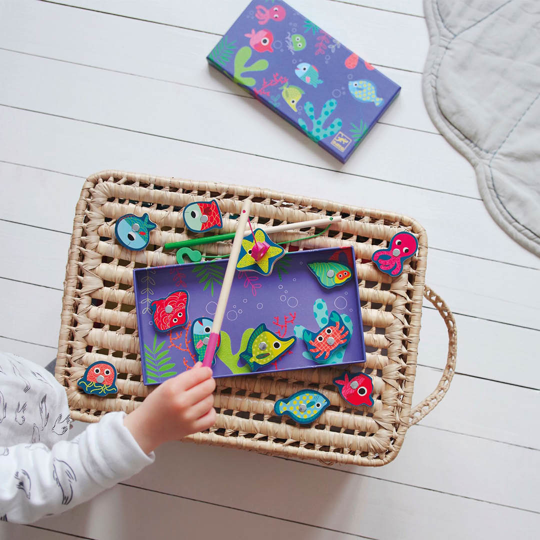 Een kinderhand speelt met het Djeco magnetisch visspel, waarbij een hengel boven de kleurrijke houten zeedieren in een mand wordt gehouden.