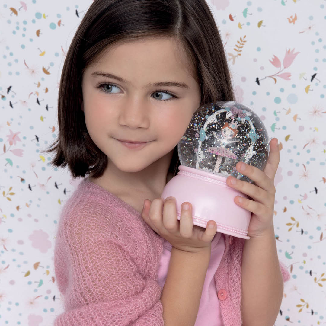 Een meisje houdt het Djeco ballerina nachtlampje vast tegen een bloemenbehang.