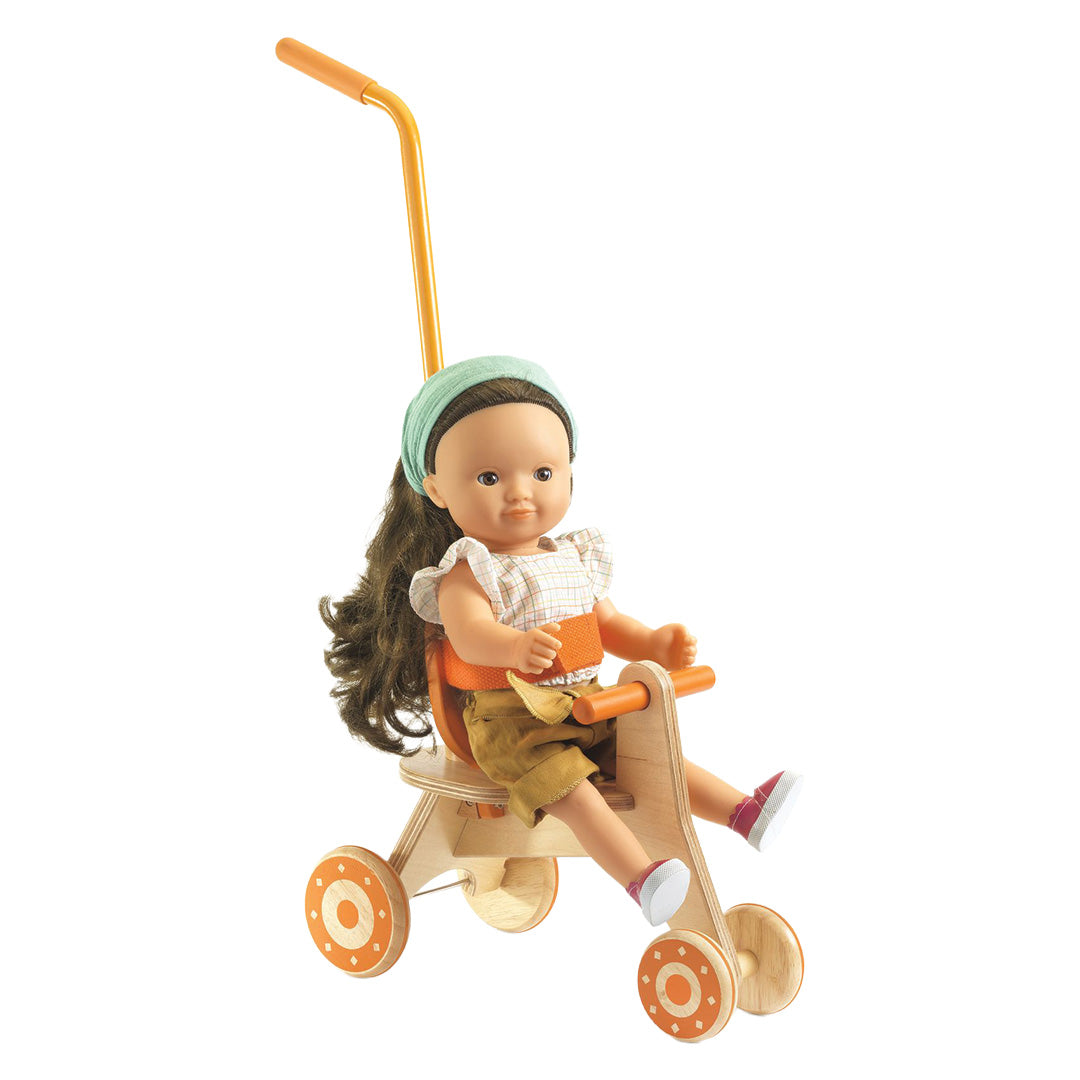 Een pop met bruin haar zit op de Djeco houten poppendriewieler.