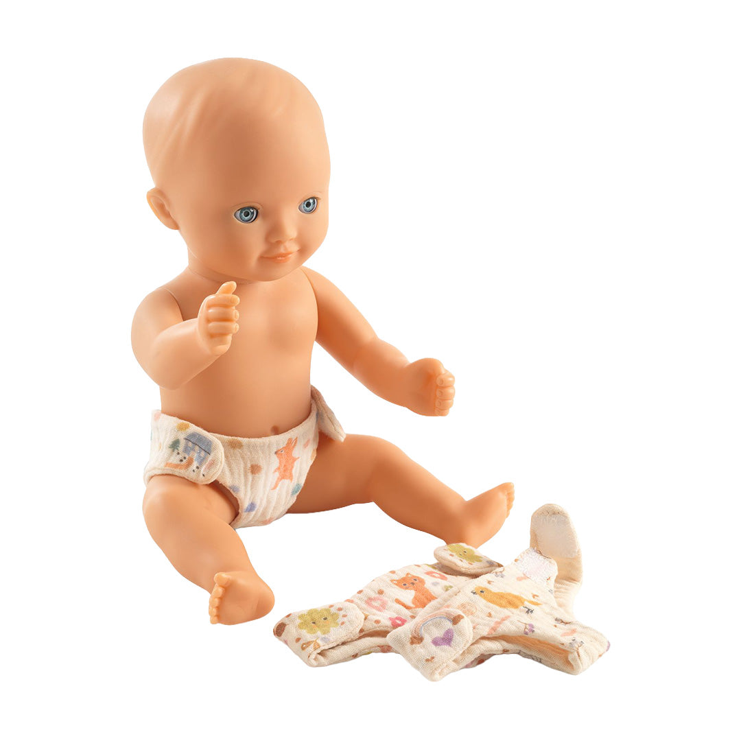 Een zittende babypop draagt een Djeco Pomea stoffen luier, met een andere luier ernaast.