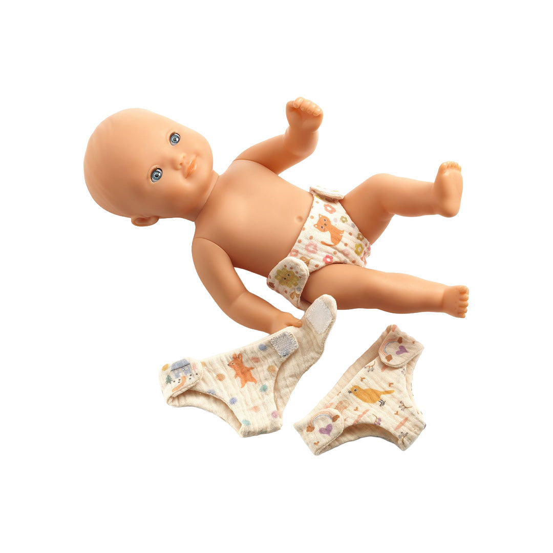 Een liggende babypop draagt een Djeco Pomea stoffen luier, met twee andere luiers ernaast.