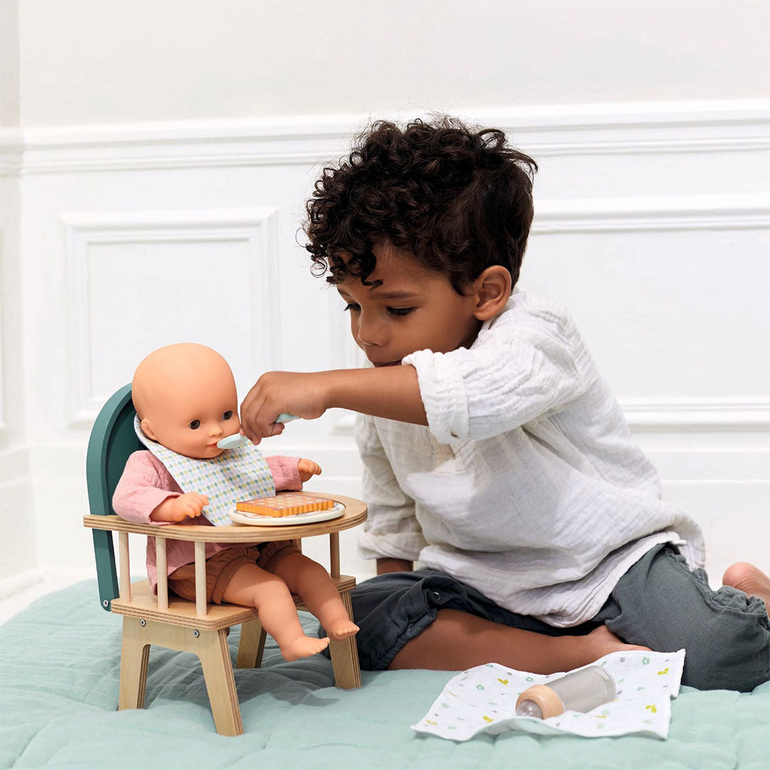 Een kind geeft een pop eten met een lepel in de Djeco houten poppenstoel.
