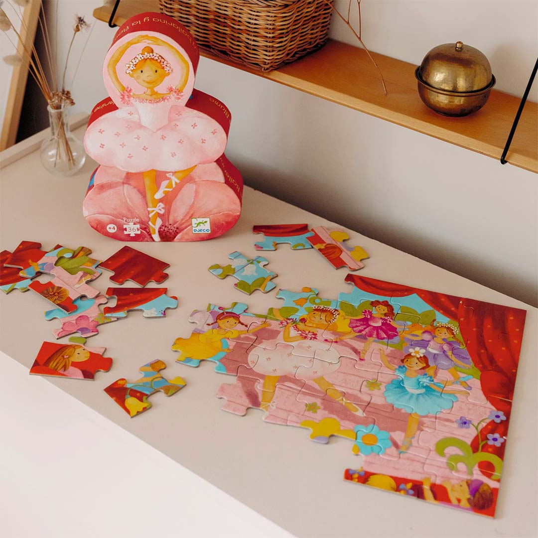 Djeco legpuzzel met ballerinas op een podium, deels in elkaar gezet, naast de ballerina-vormige verpakking.