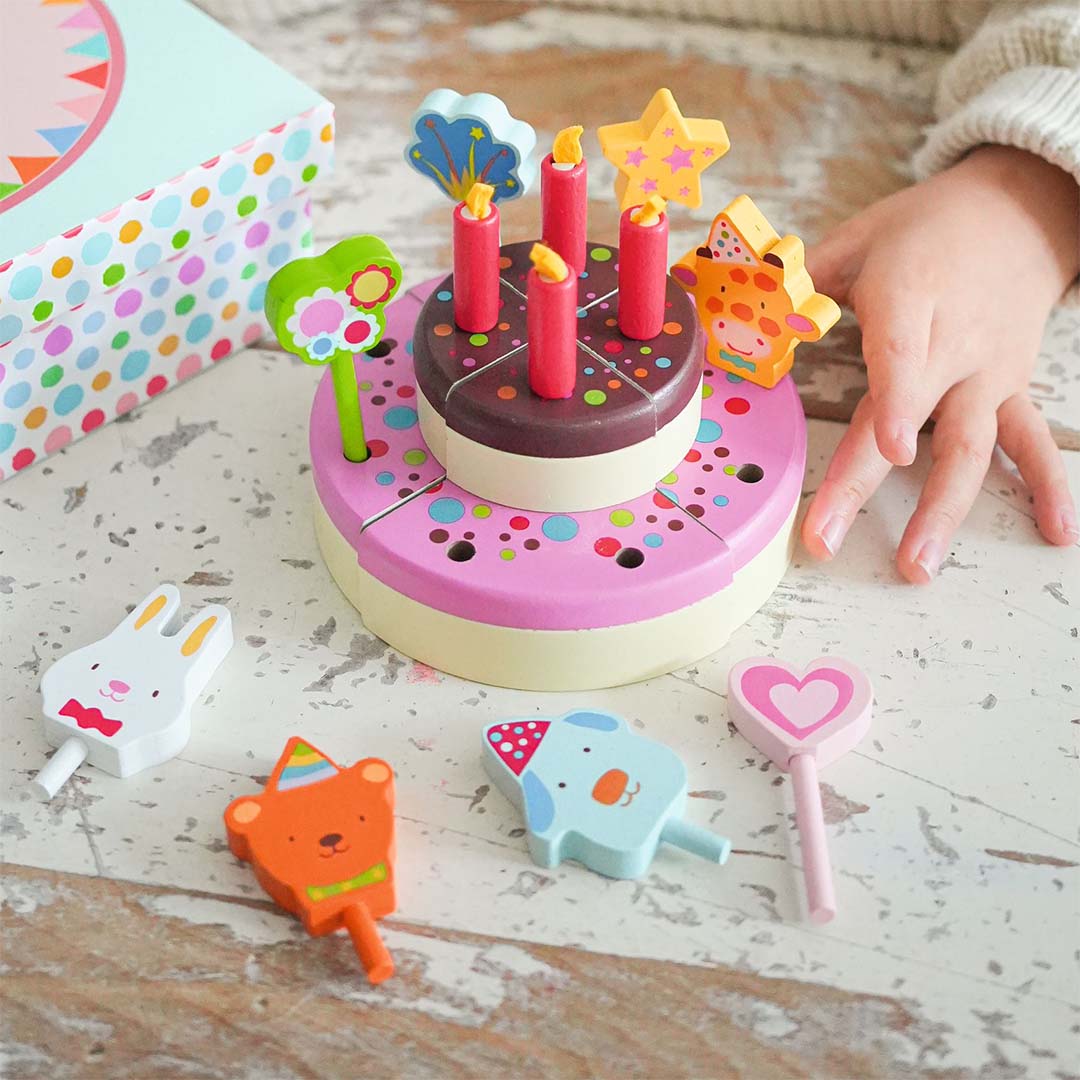 Een kinderhand reikt naar de Djeco houten speelgoed verjaardagstaart met kaarsen en toppers.