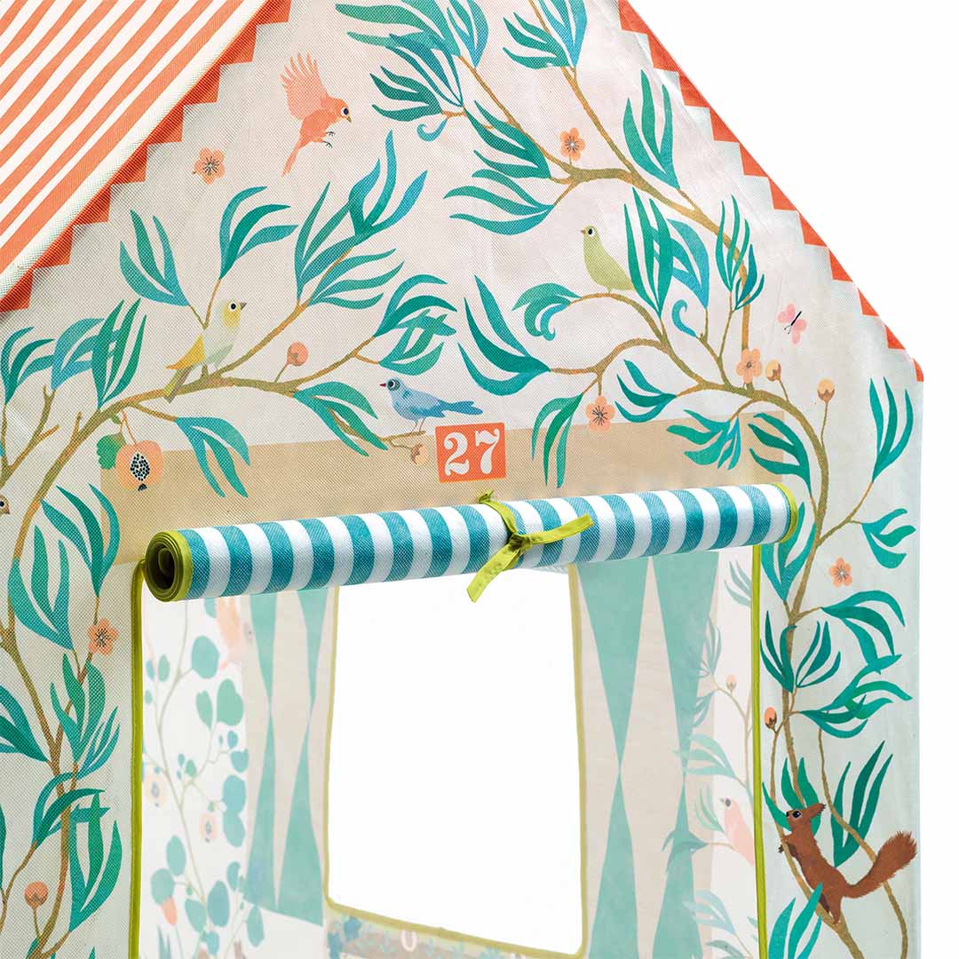 Detail van het Djeco speelhuis met een raam, opgerold gordijn en decoratie van bladeren en vogels.