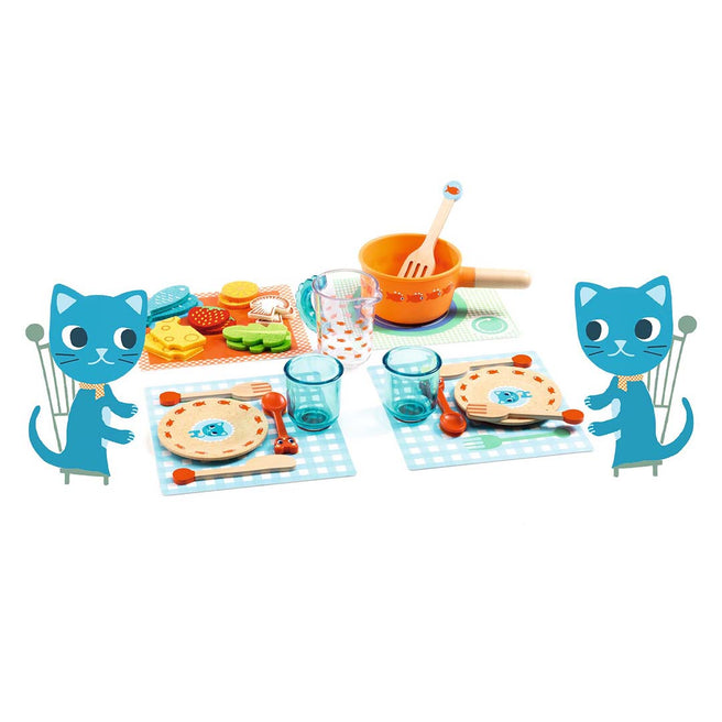 Djeco speelservies met twee gedekte plaatsen, een pan en diverse speelvoedsel, geflankeerd door twee kattenillustraties.