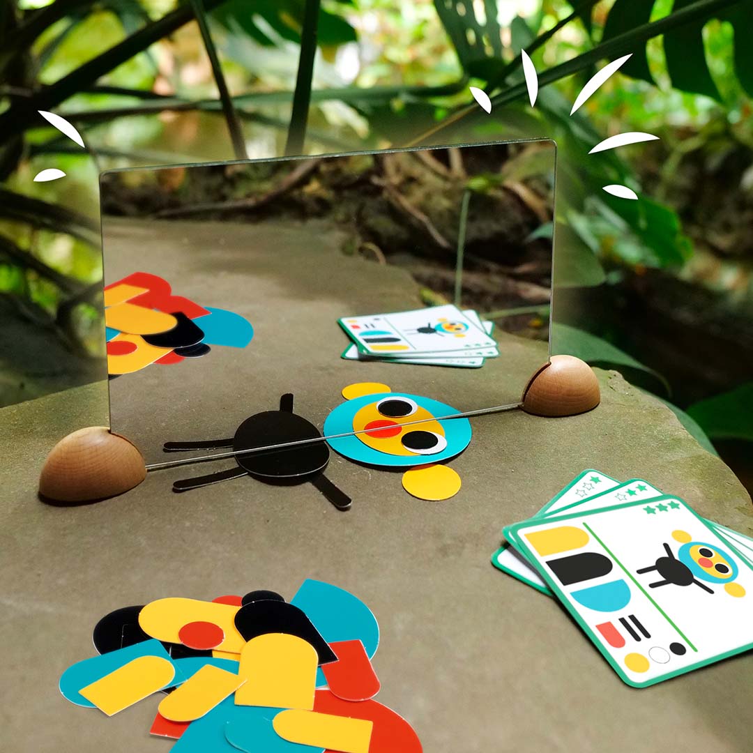 Djeco Ze Mirror Animals educatief spiegelspel met een spiegel en vormen die een zwart insect vormen, buiten op een steen.