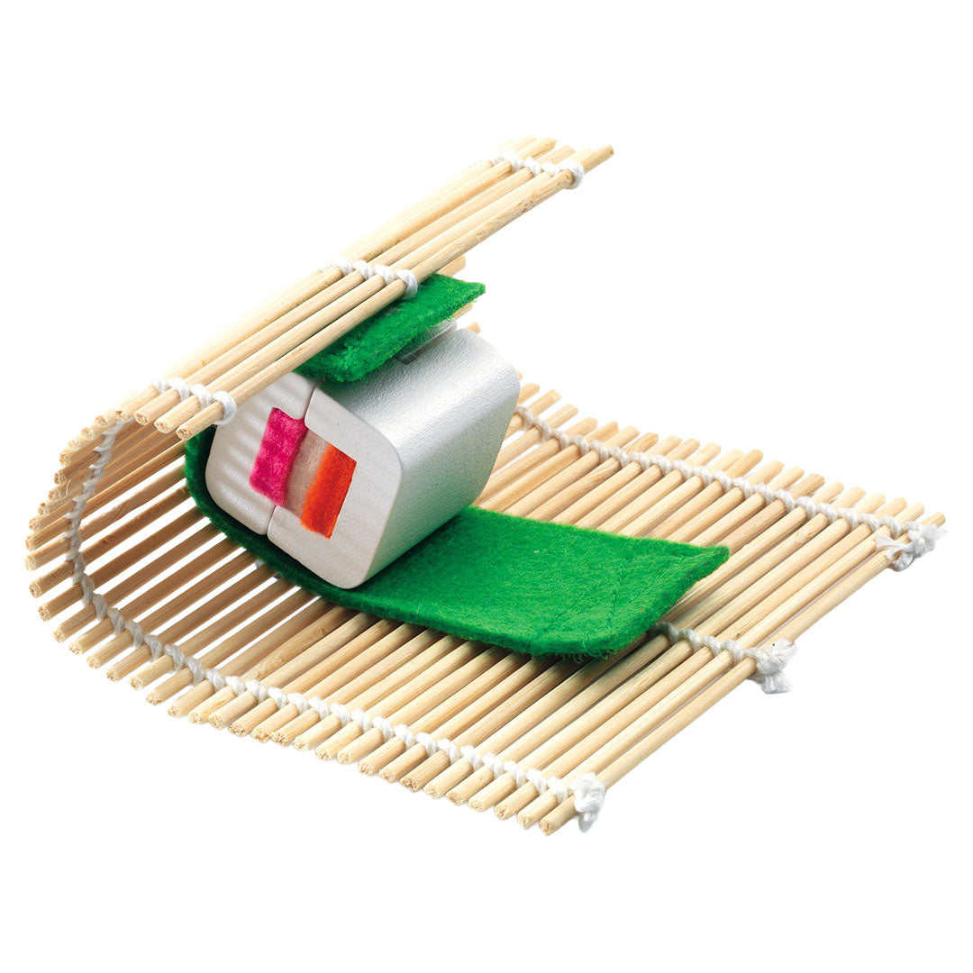 Een houten speelgoed sushirol met groen vilt wordt op een bamboe rolmatje gerold.