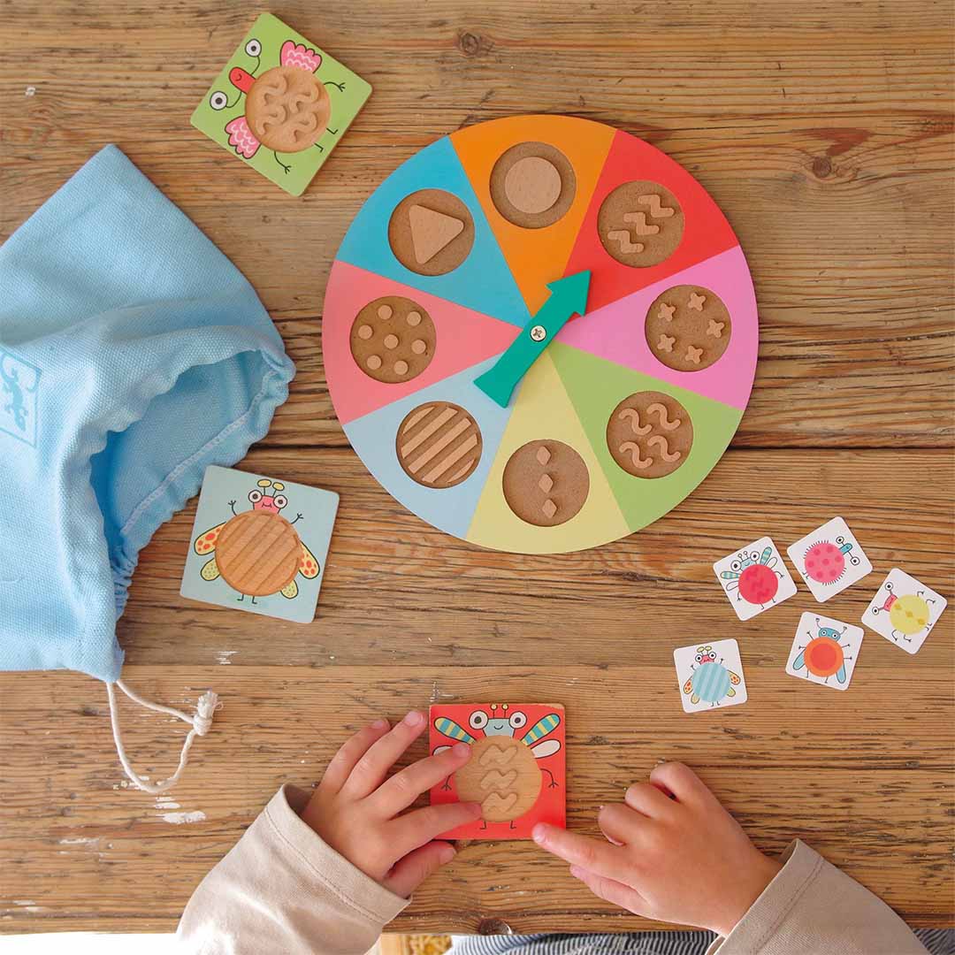 Kind speelt met het Djeco Tactil Bzzz tactiel spel met kleurrijke spinner en insectentegels op een houten tafel.