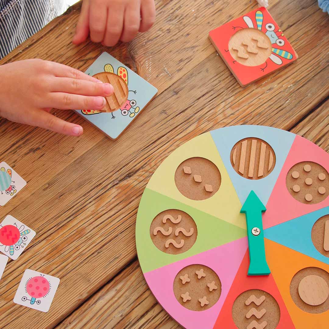 Kind raakt een tactiele insectentegel aan van het Djeco Tactil Bzzz spel naast de kleurrijke spinner.