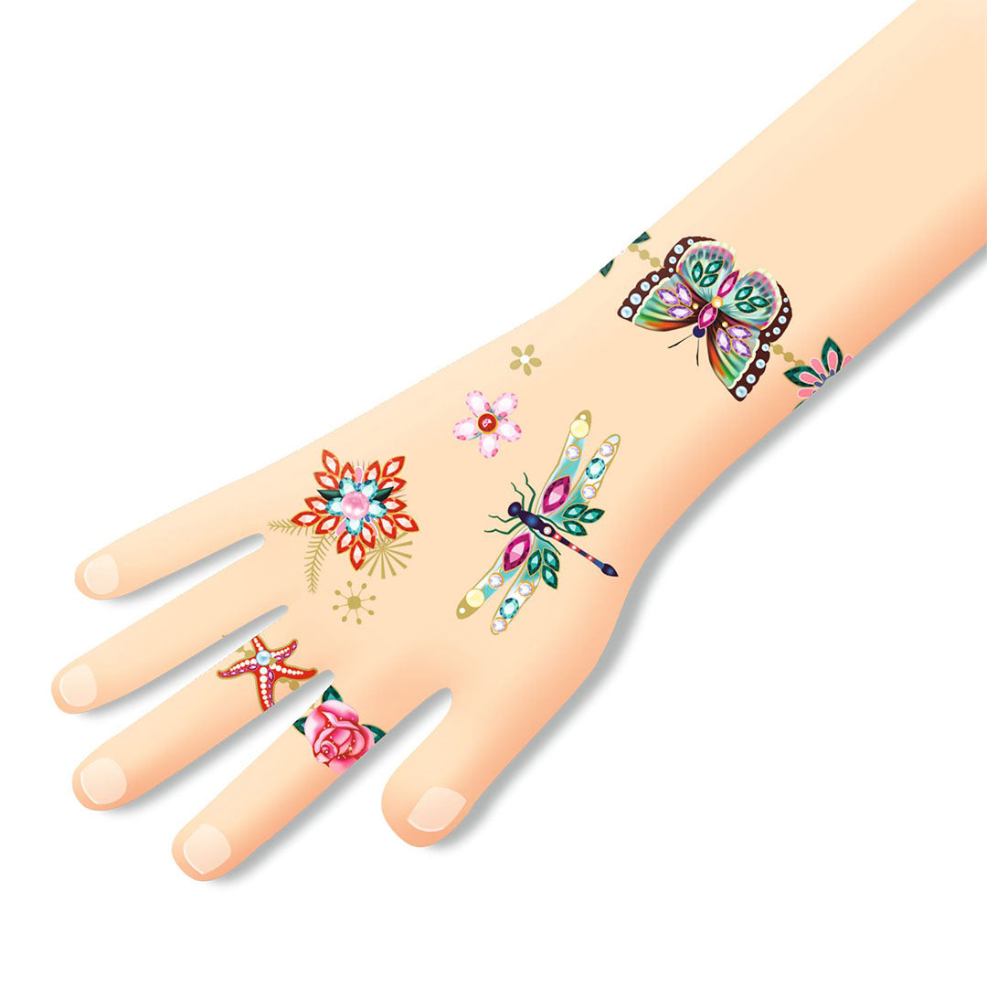 Een hand met daarop aangebrachte tijdelijke tattoos van vlinders, libellen, bloemen en sieraden.