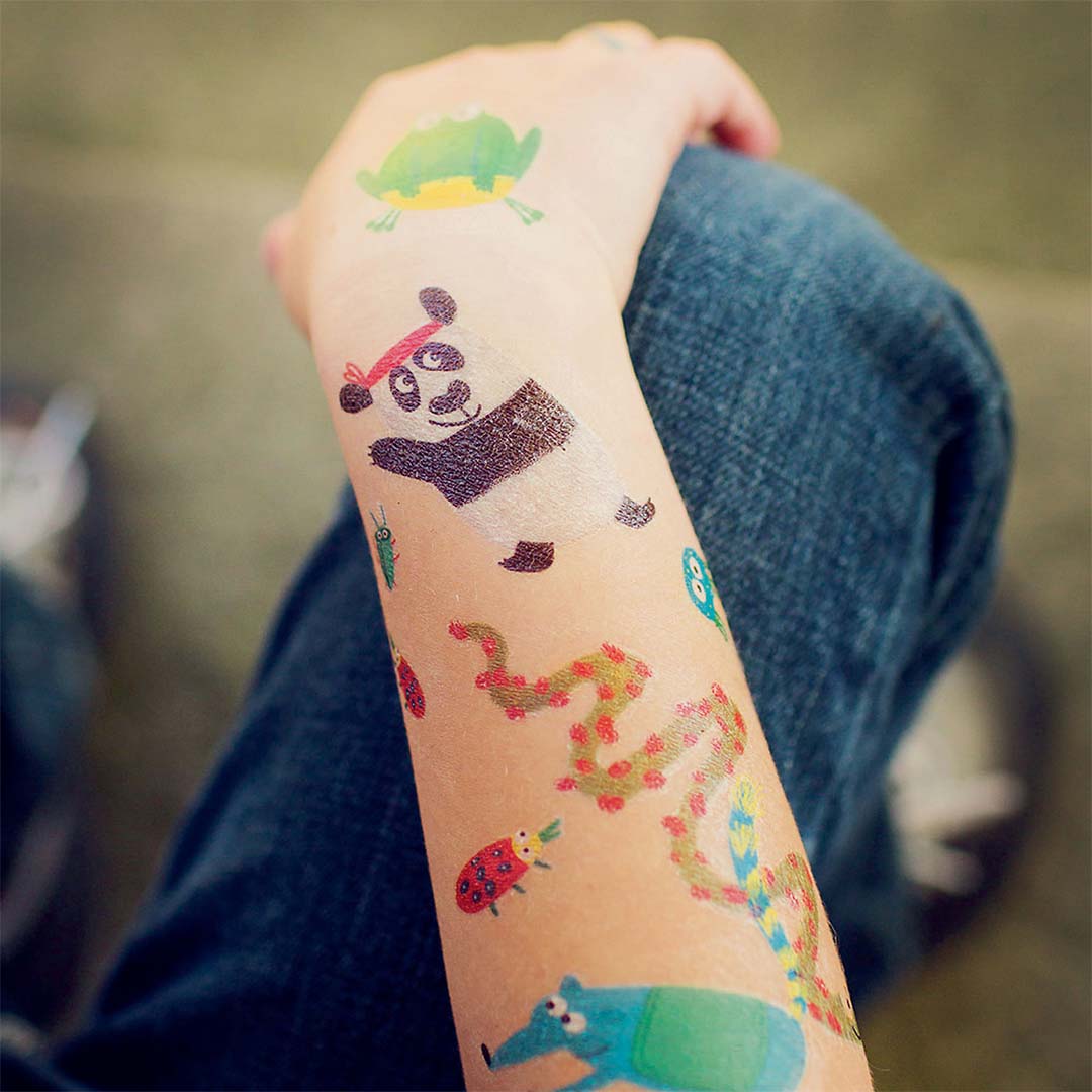 Een arm met daarop verschillende kleurrijke dierentattoos, waaronder een panda en een kikker.