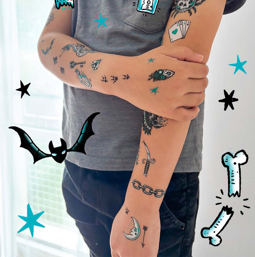Een kinderarm met diverse Djeco tijdelijke tatoeages, waaronder een vleermuis, maan en zeerovers- en dierenmotieven.