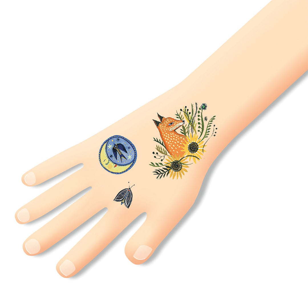Een hand met drie aangebrachte tijdelijke kindertatoeages: een vos, een maan met sterren en een mot.