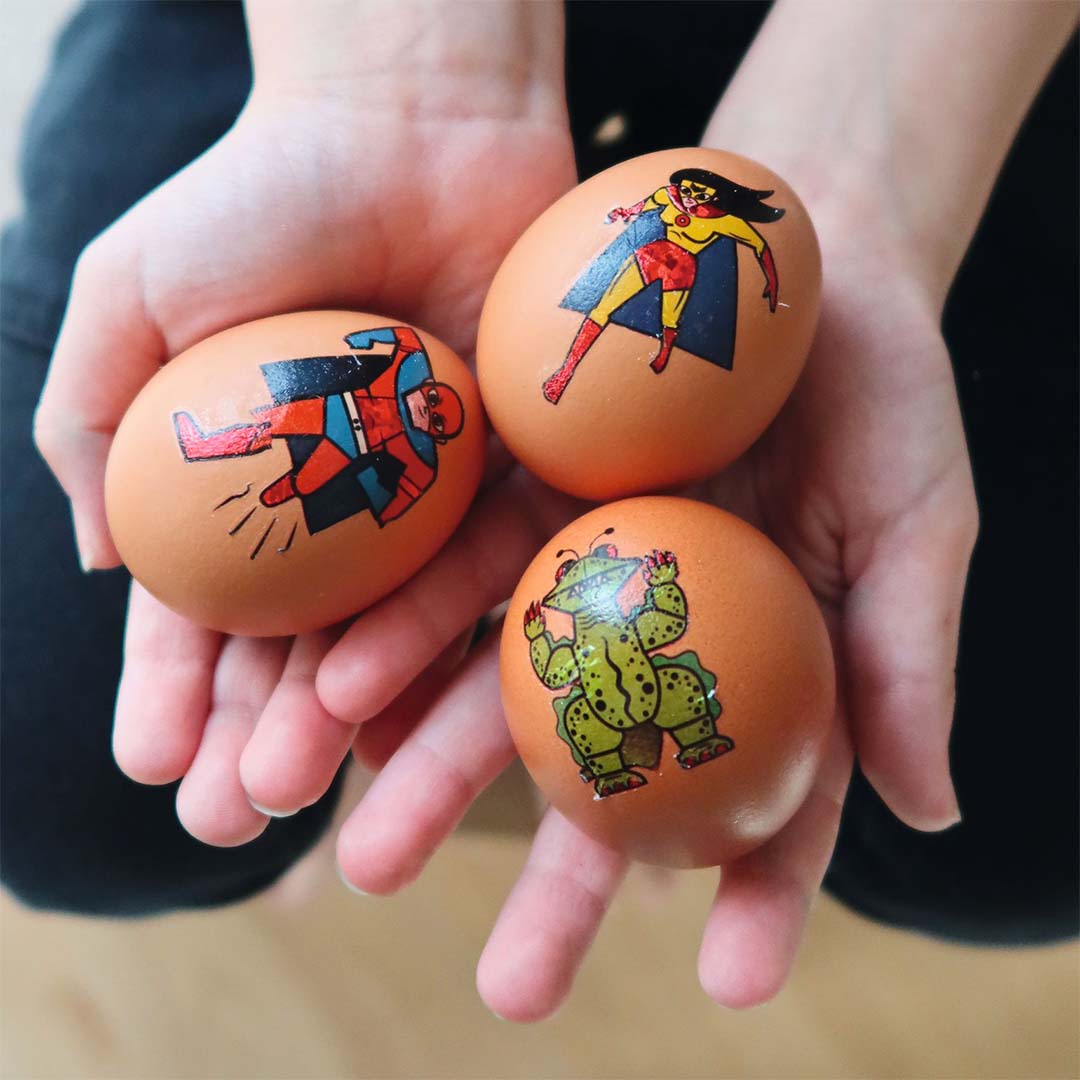 Drie bruine eieren met tijdelijke superhelden en schurken tattoos, vastgehouden in twee handen.