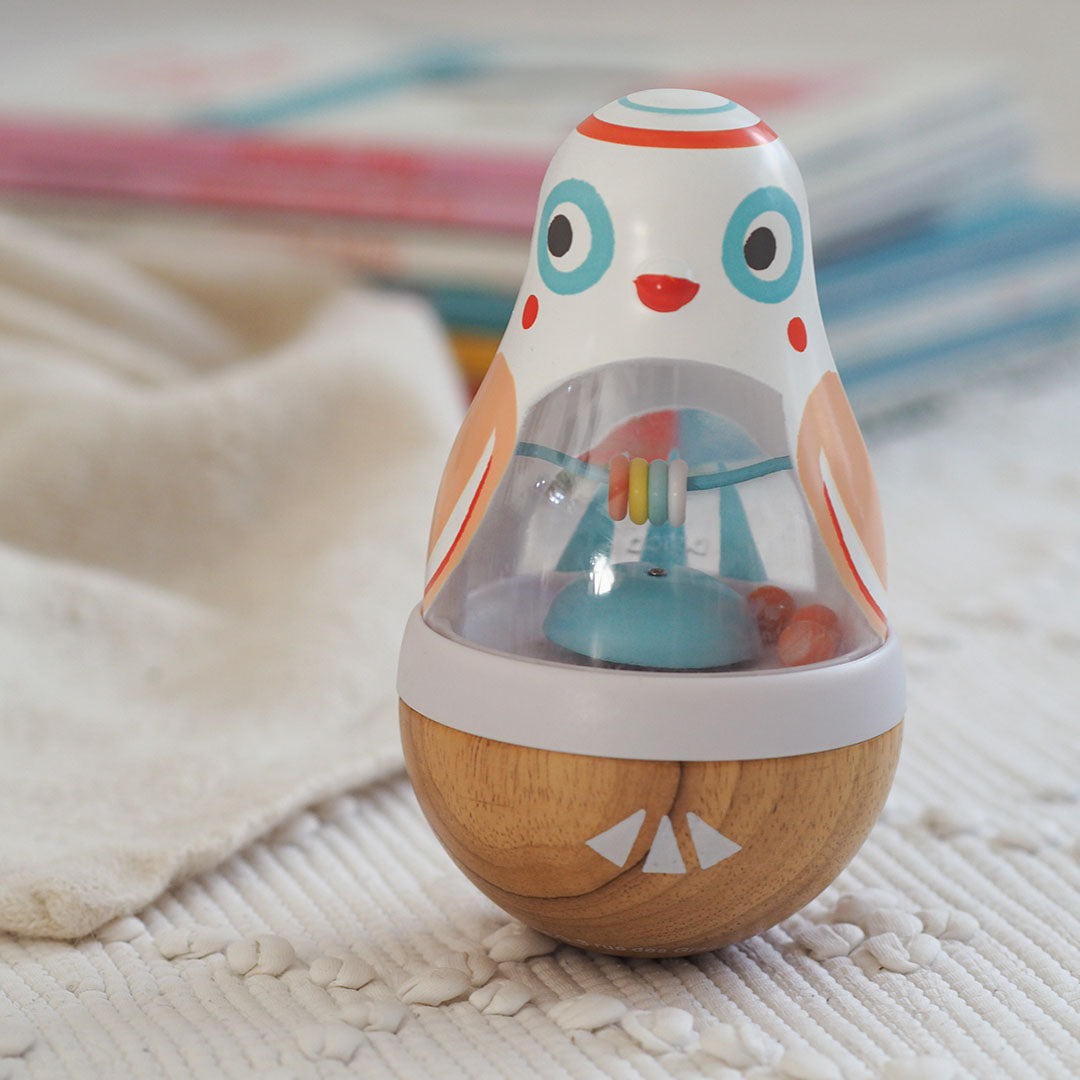 Djeco Baby Poli tuimelaar in de vorm van een vogel op een wit kleed.