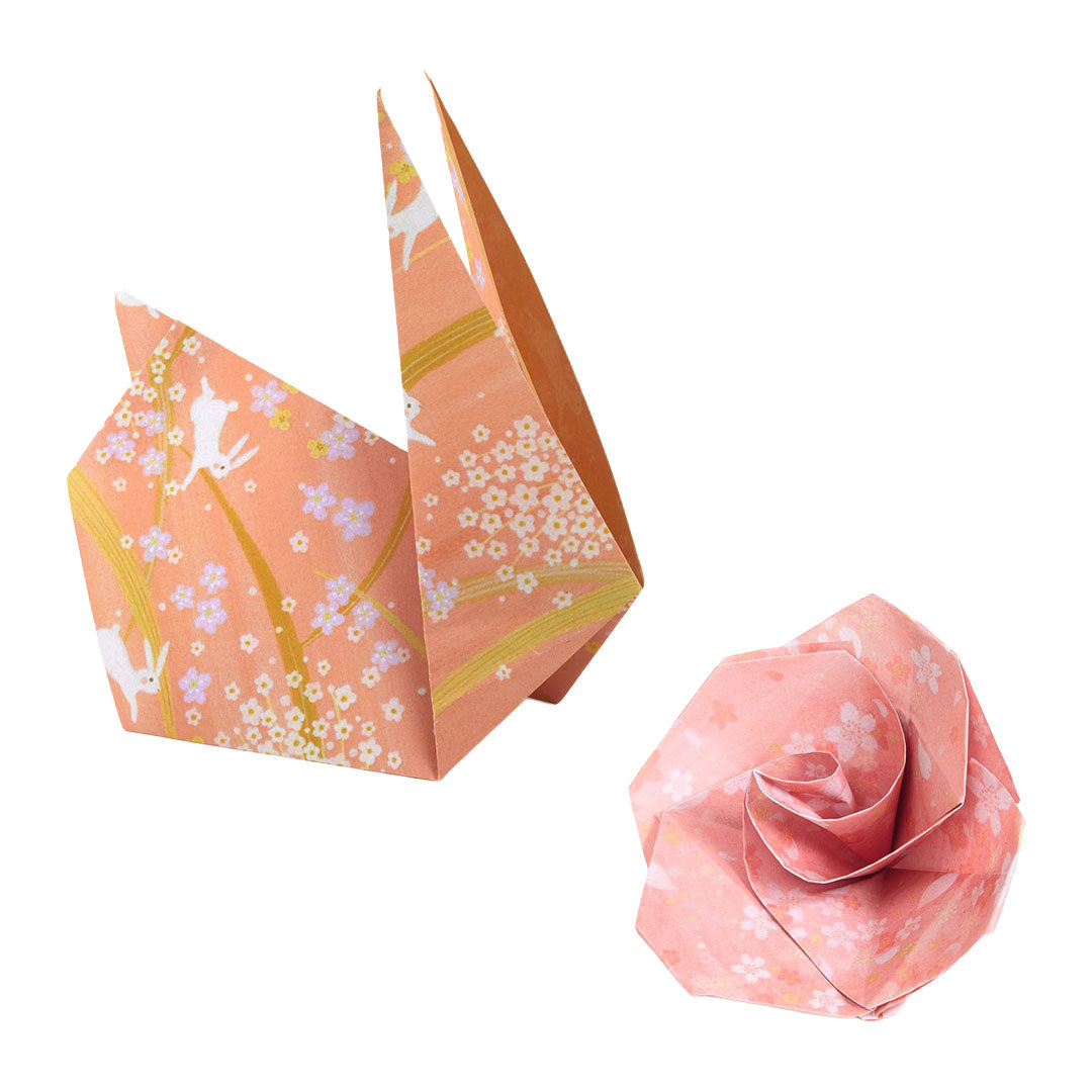 Twee gevouwen origami figuren: een oranje konijn of vogel en een roze roos, beide met bloemenpatronen.