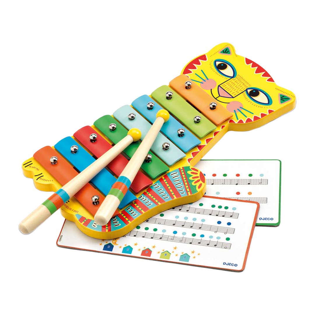 Djeco xylofoon in de vorm van een gele kat met kleurrijke toetsen en twee stokjes, liggend op twee muziekkaarten.