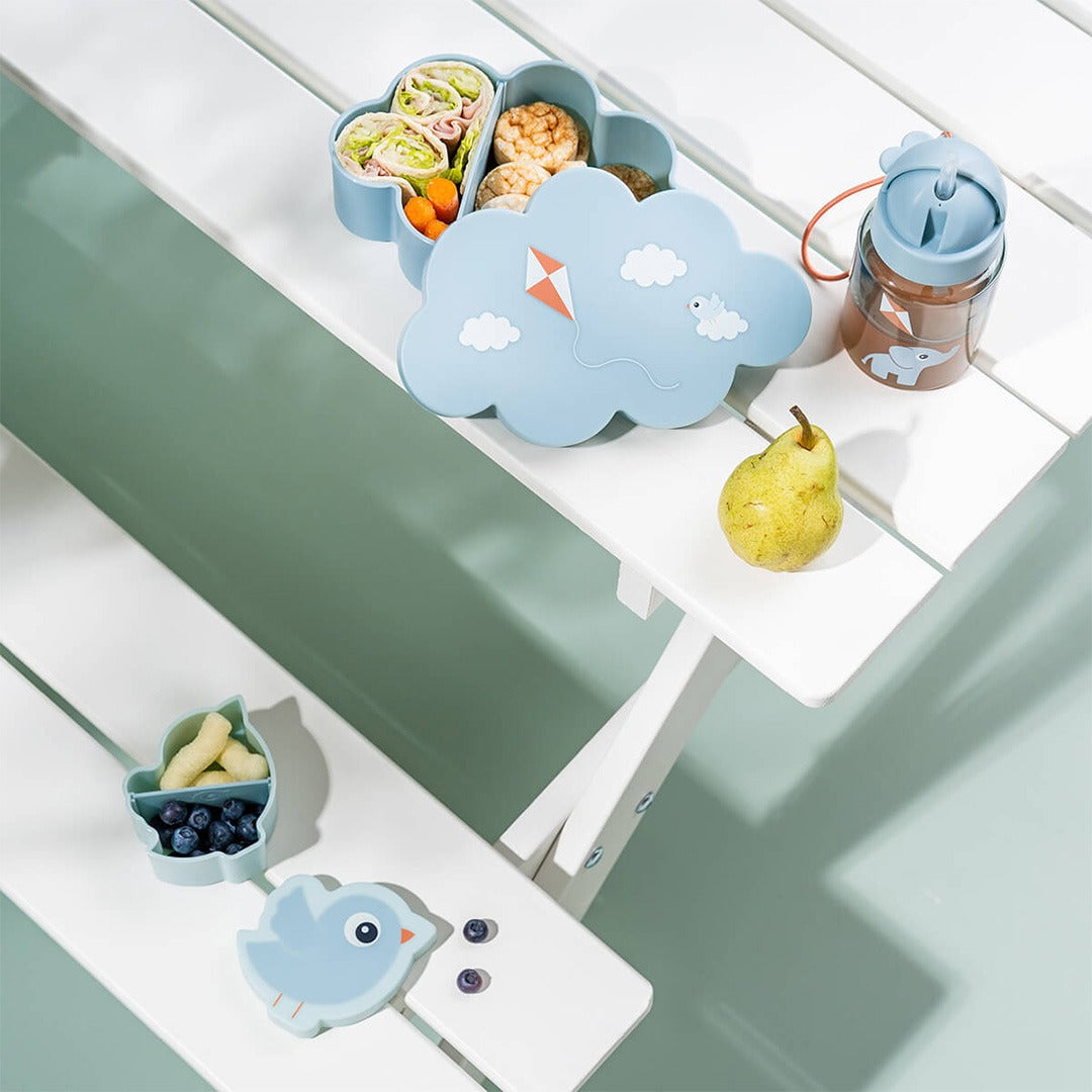 Done by Deer kinder lunchset met open wolk-broodtrommel gevuld met lunch, open vogel-snackdoos met blauwe bessen en een drinkfles op een witte bank.