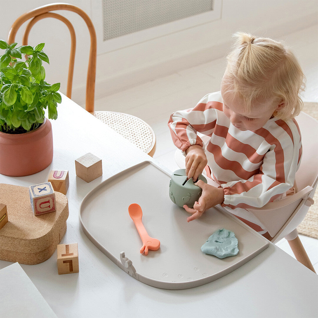 Een kind draagt de gestreepte mouwslab tijdens het spelen aan tafel.