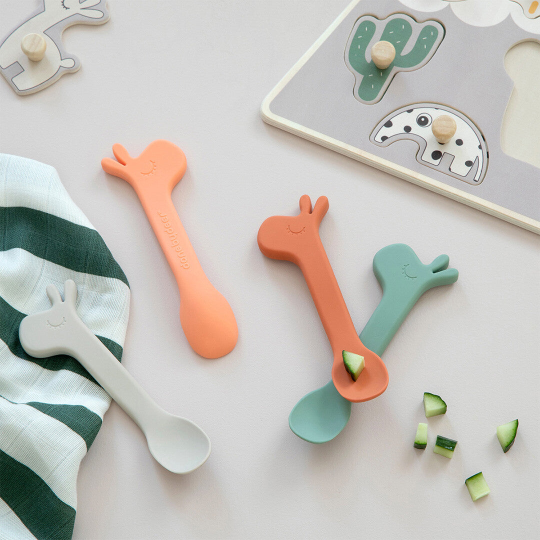 Drie Done by deer siliconen kinderlepels in verschillende kleuren met giraffehoofd, gebruikt voor het eten van komkommerstukjes.