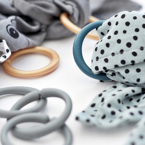 Close-up van done by deer babyspeelringen, waaronder een blauwe ring met stippenstof en grijze plastic ringen.