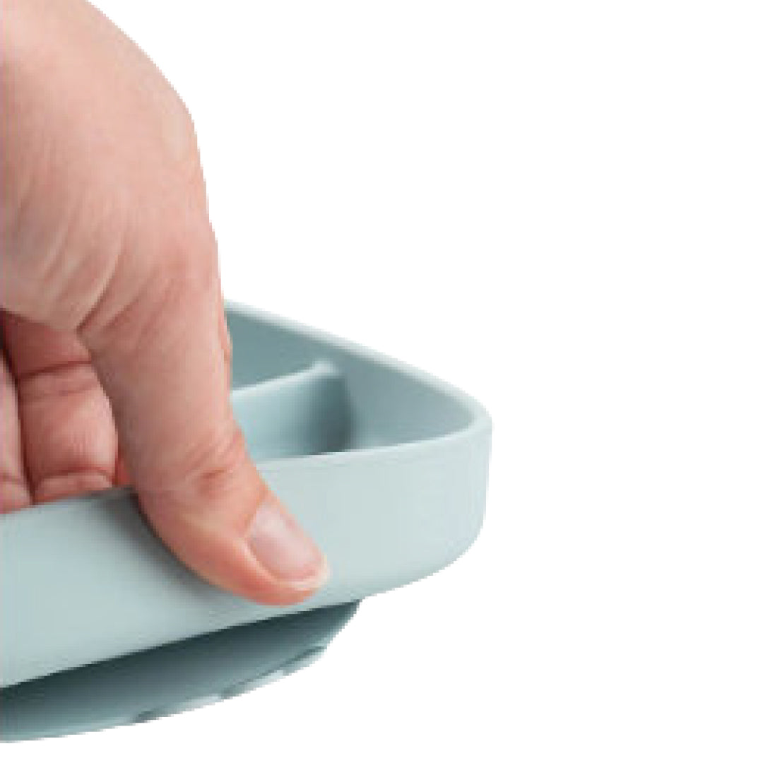 Een hand houdt de rand van het blauwe siliconen babybord vast, wat het materiaal en de dikte toont.