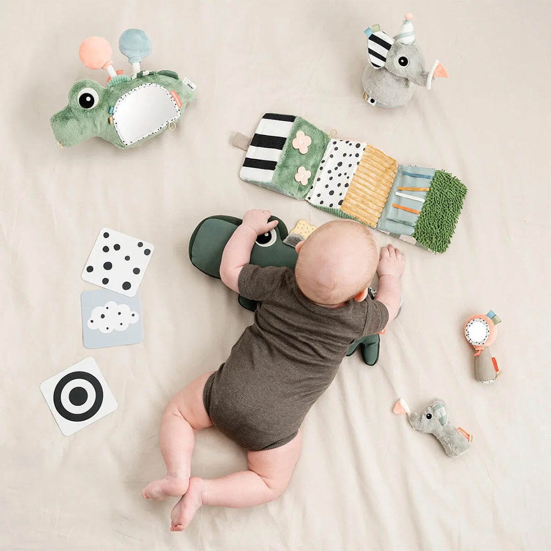 Een baby speelt op een deken met diverse done by deer babyspeeltjes, waaronder de groene krokodil activiteitenspiegel.