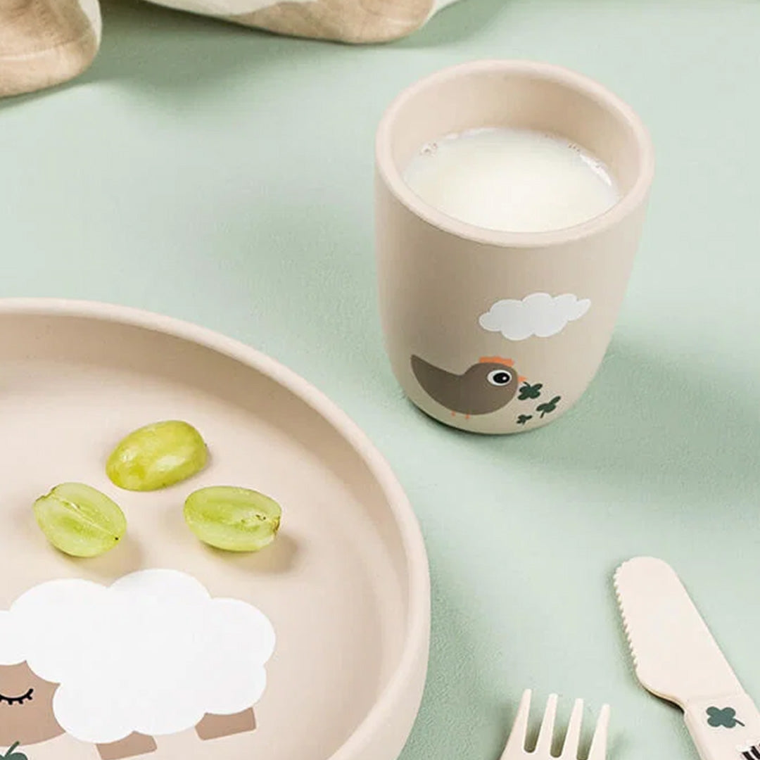 Done by deer kinderbeker met melk, staand naast een bijpassend bord met druiven en bestek.