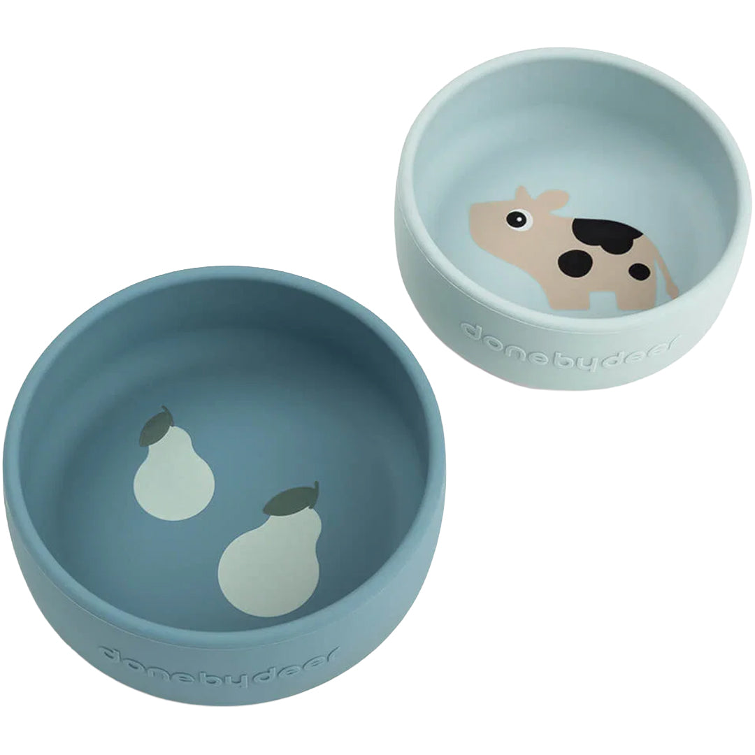 Twee Done by Deer siliconen kinderkommen, één blauw met peren en één lichtblauw met een koe.