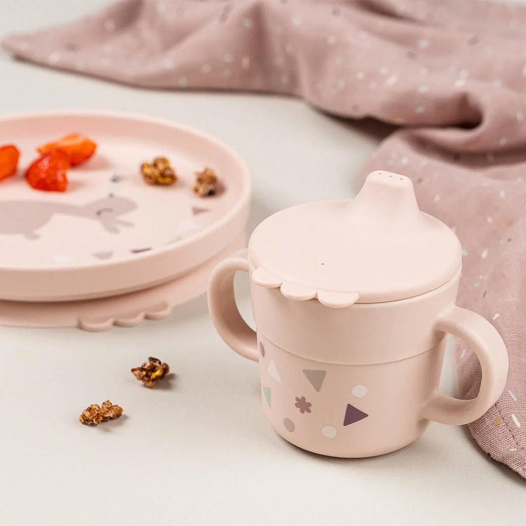 Een roze done by deer kindersippybeker met geometrische patronen staat naast een bijpassend bord met konijn en snacks.