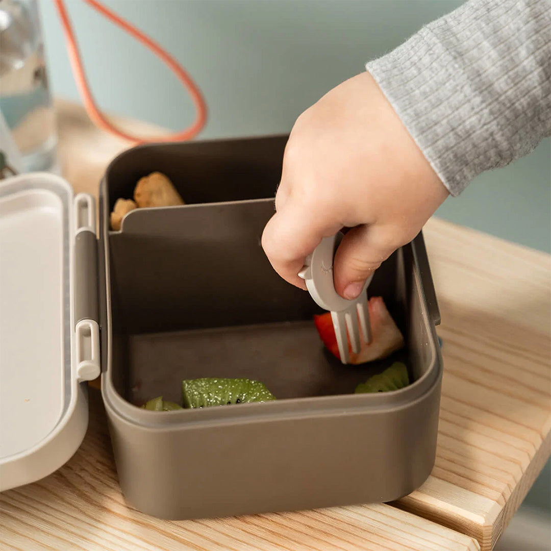 Een kinderhand gebruikt een vogel snackprikker in de open lunchbox met fruit.