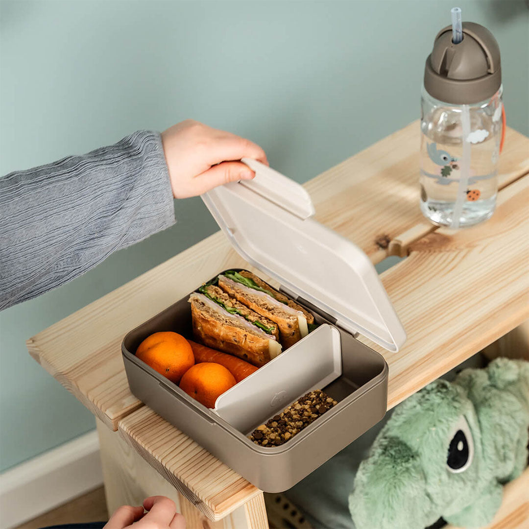 Een kinderhand opent de Done by Deer lunchbox, gevuld met brood, fruit en groenten.
