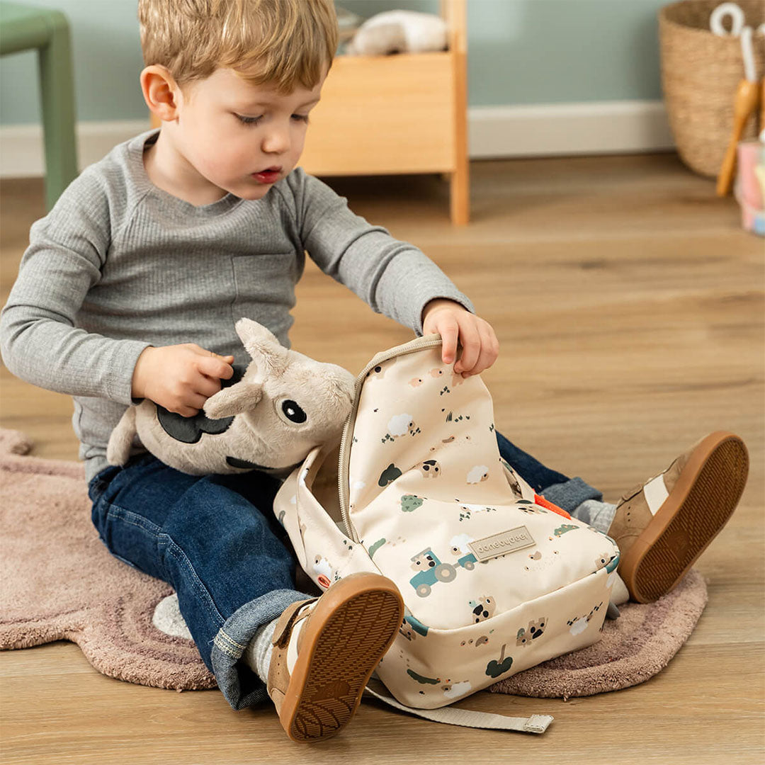 Een peuter stopt een knuffel in de open done by deer peuterrugzak met Tiny Farm patroon.