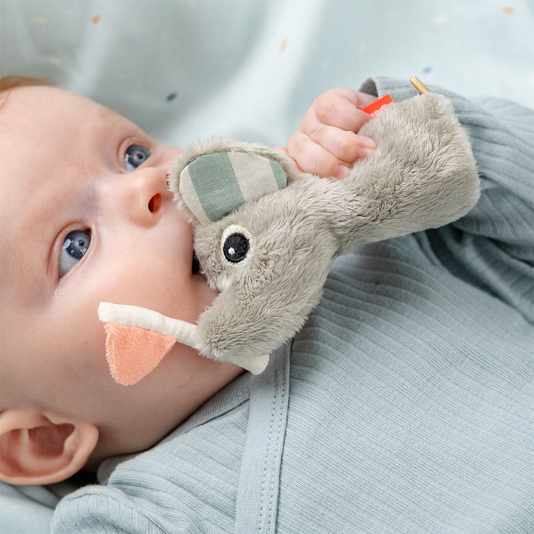 Een baby ligt op de rug en bijt op de Done by Deer olifant rammelaar.