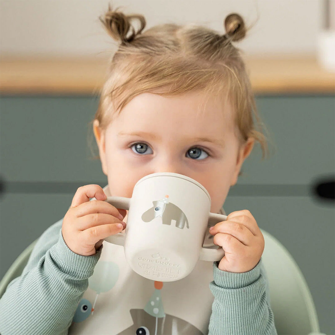 Een baby drinkt uit de done by deer siliconen tuitbeker met hippo-thema.