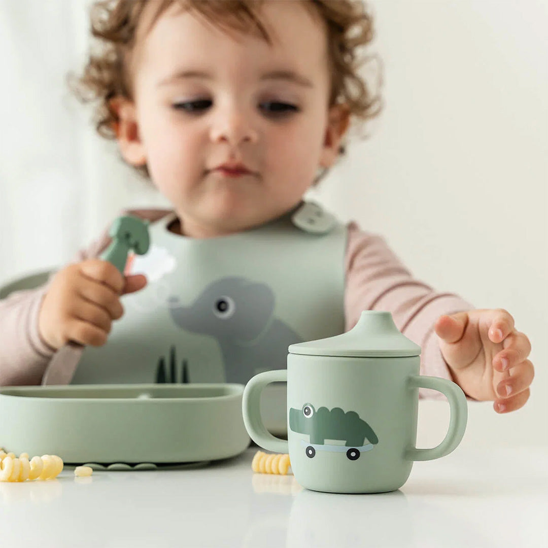 Een baby zit aan tafel met de done by deer groene tuitbeker en bijpassende kom.