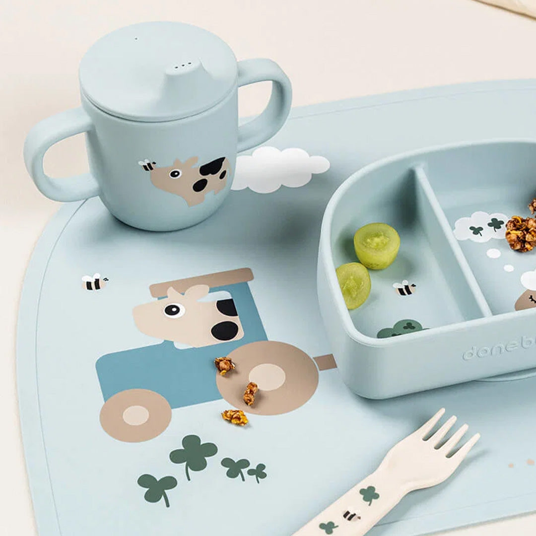 Done by deer siliconen babytuitbeker op een placemat met een tractor, samen met een bijpassend bord en vork.