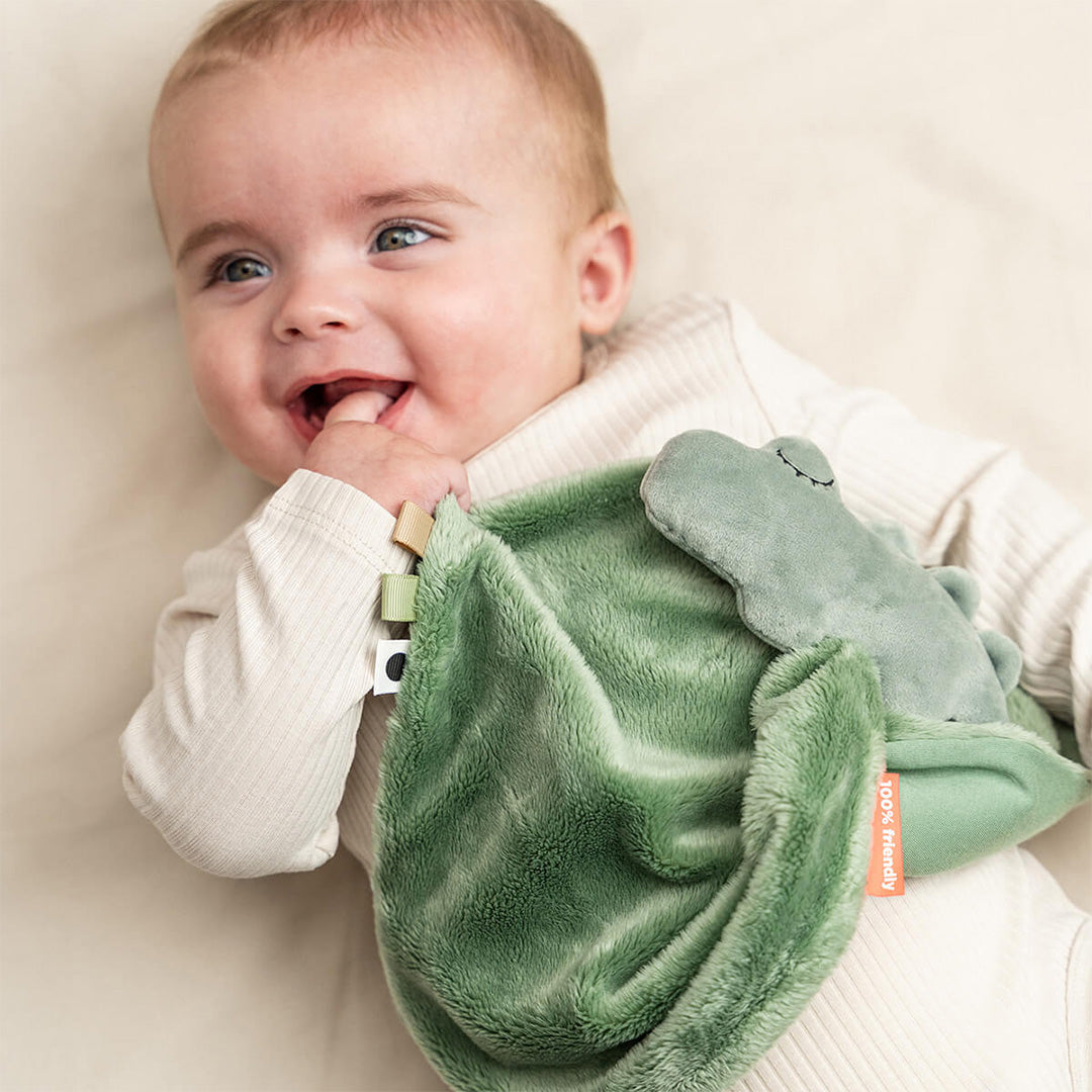 Een lachende baby speelt met de Done by Deer groene krokodil babyspeendoek.