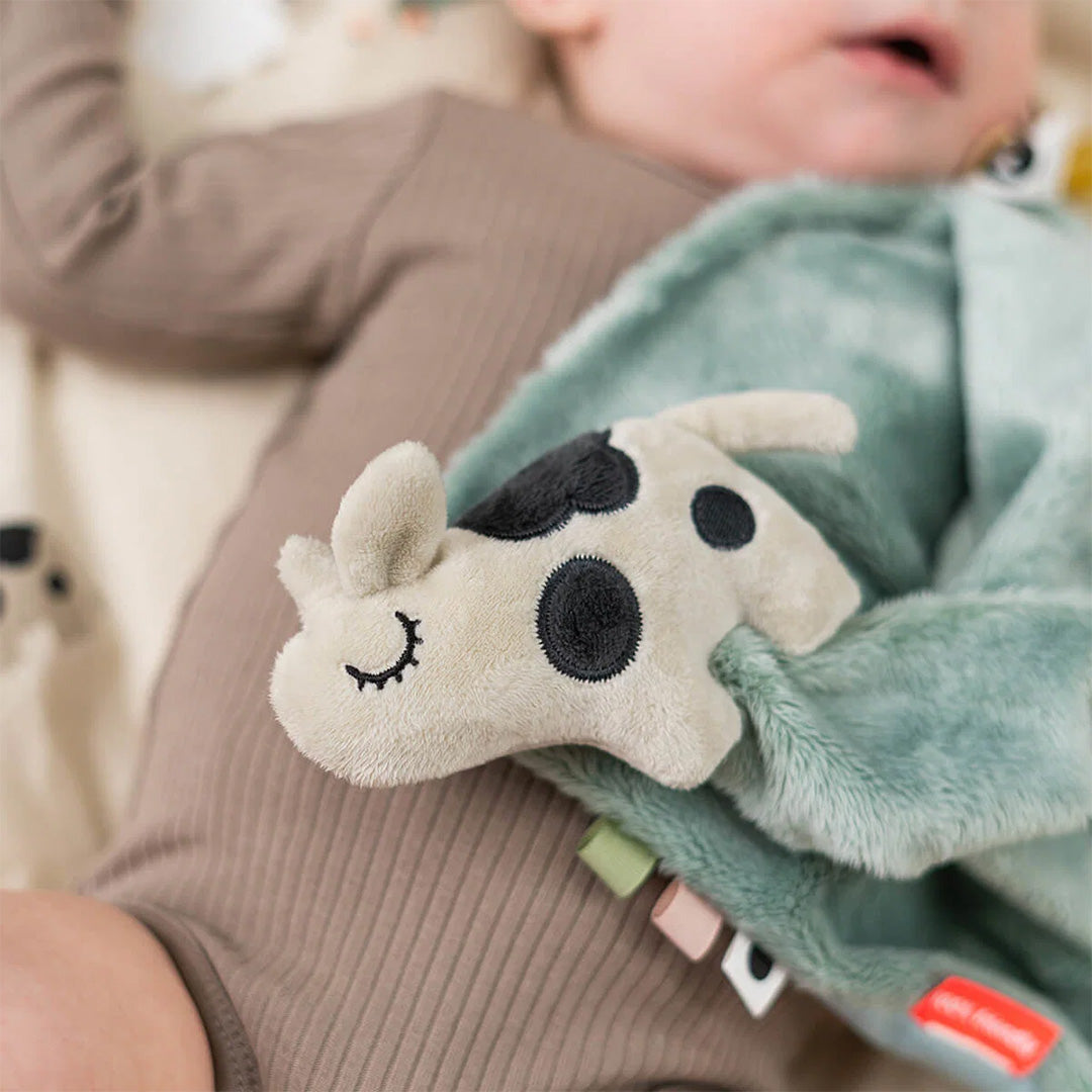 Detailfoto van de Done by Deer pluche koeienkop op de groene speendoek, vastgehouden door een baby.