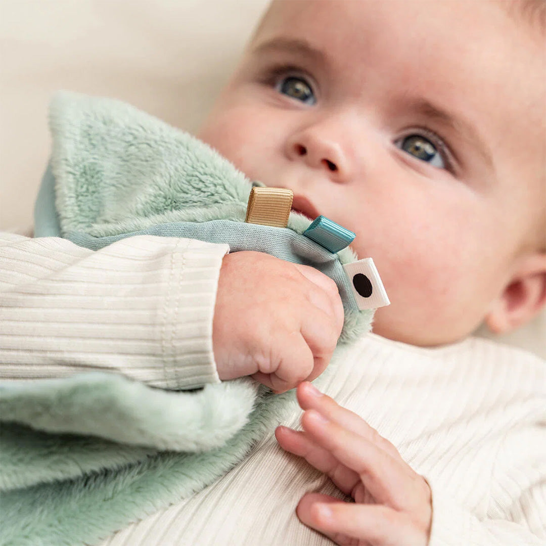Een babyhandje houdt een hoek van de Done by Deer groene Elphee speendoek vast.