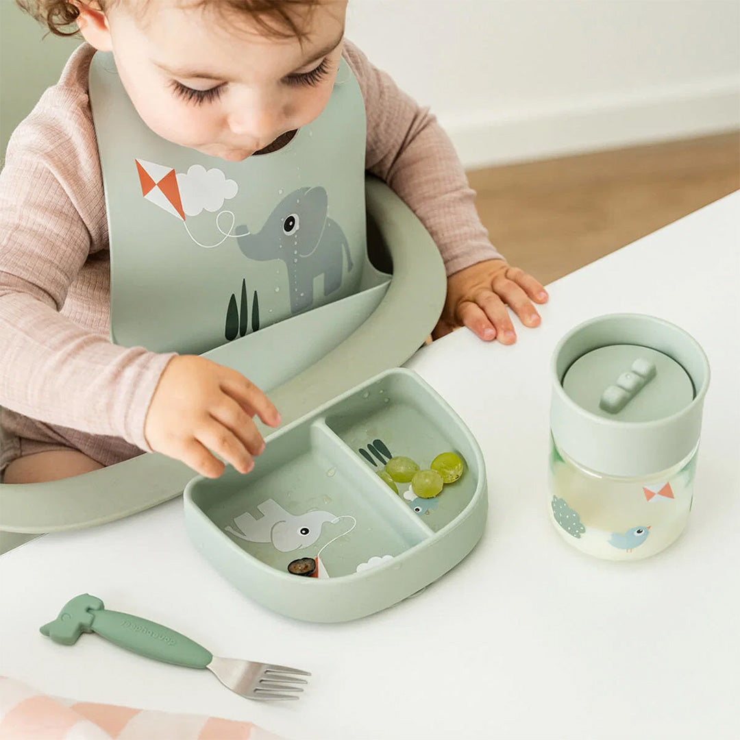 Baby zit aan tafel met een Done by Deer groen siliconen vakjesbord met olifant en een bijpassende slab en beker.