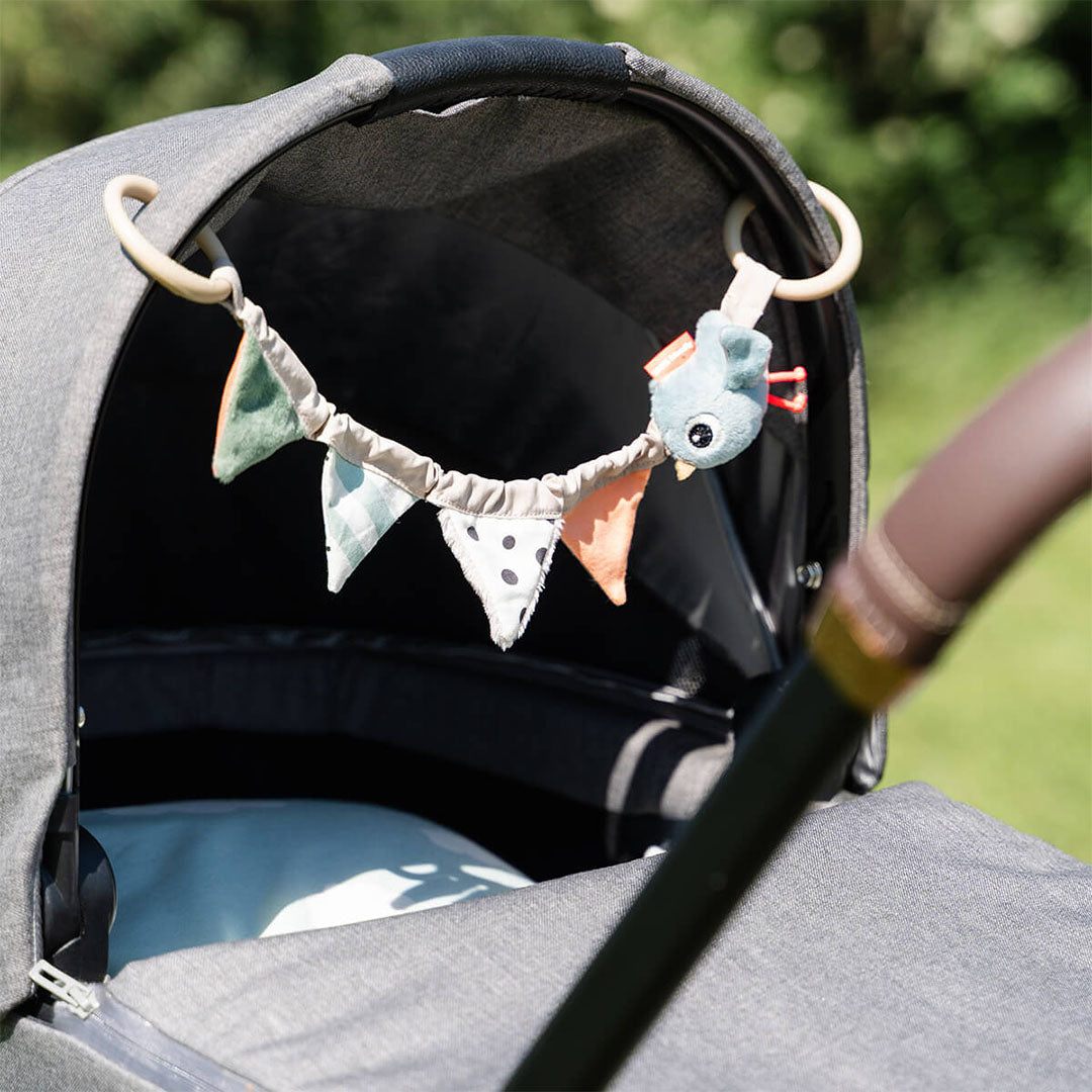 De Done by Deer wagenspanner met vogel en vlaggetjes hangt in een grijze kinderwagen.